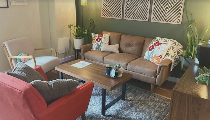 A cozy living room with a brown leather sofa, red armchair, wooden coffee table, potted plants, and decorative wall art above the sofa. representing Vitality Nutrition with Rachel Green in Ohio
